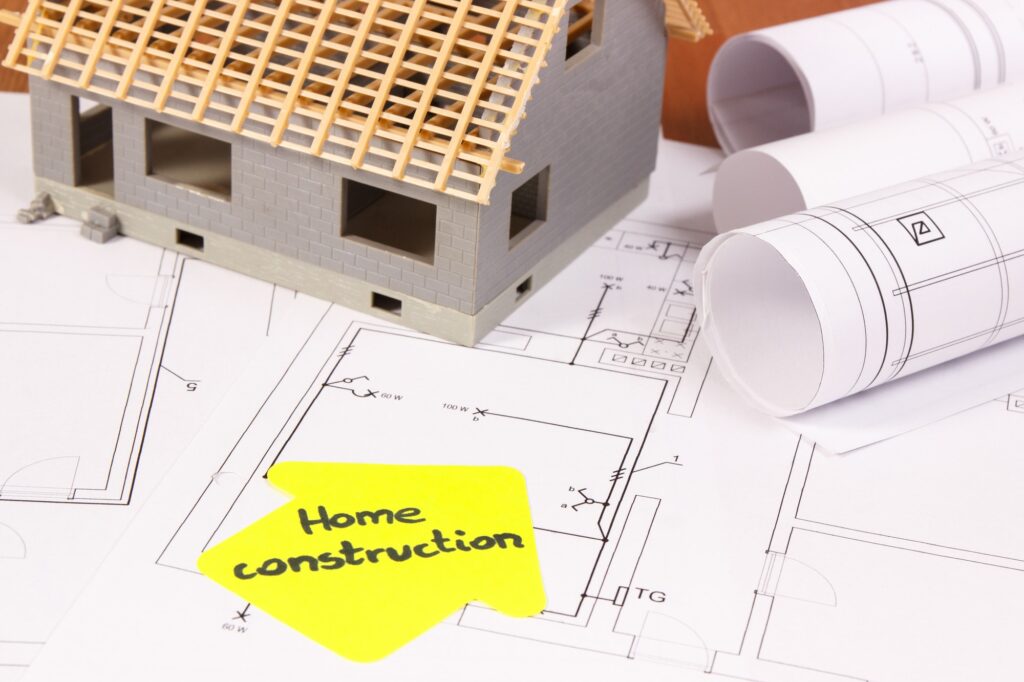 House under construction and rolls of electrical diagrams or blueprints, building home concept